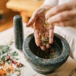 Home Close-up of herbs being prepared in a mortar and pestle by a woman, showcasing natural remedy techniques.