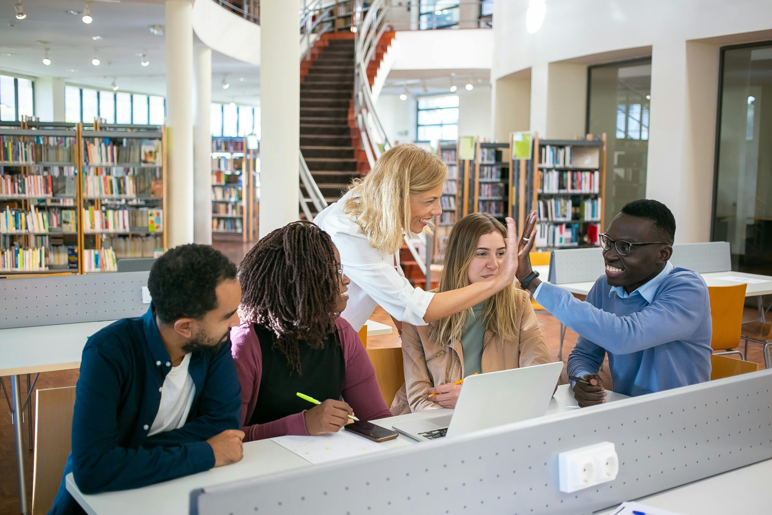 A group of multiethnic college students collaborating on a project in a modern library setting.