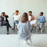 Home People engaging in a group therapy session indoors, discussing mental health topics.